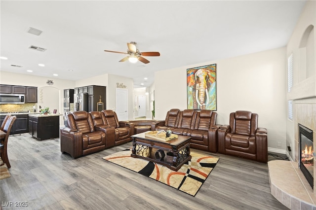 living area featuring visible vents, a ceiling fan, light wood-style flooring, and a tiled fireplace
