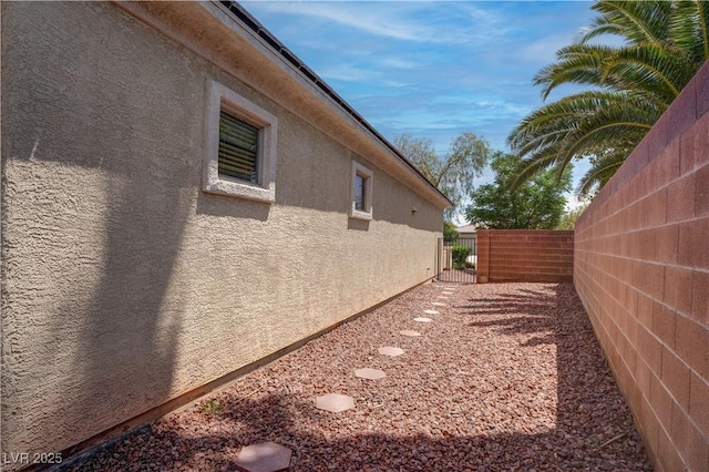 view of side of home featuring a gate, stucco siding, and fence