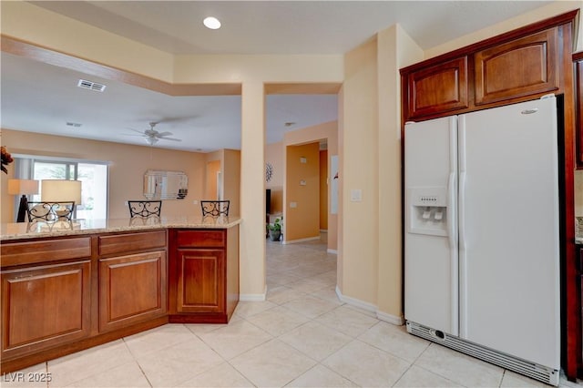 kitchen featuring a ceiling fan, visible vents, white refrigerator with ice dispenser, light tile patterned floors, and light stone counters