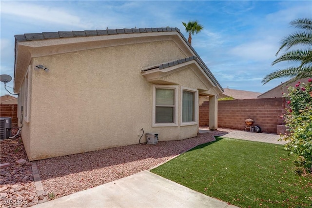 rear view of house featuring fence, stucco siding, cooling unit, a patio, and a yard