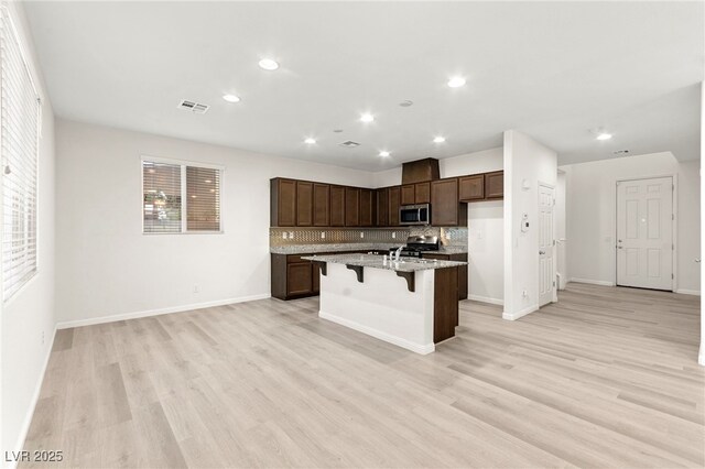 kitchen with decorative backsplash, dark brown cabinetry, visible vents, stainless steel microwave, and light wood finished floors