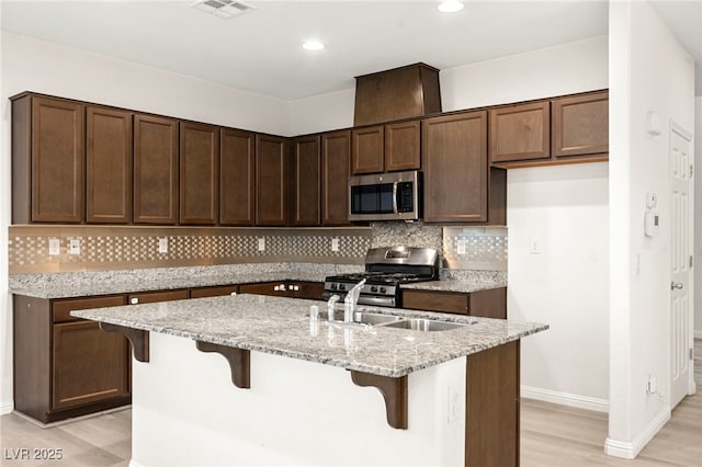 kitchen with light stone counters, stainless steel appliances, baseboards, light wood-type flooring, and tasteful backsplash