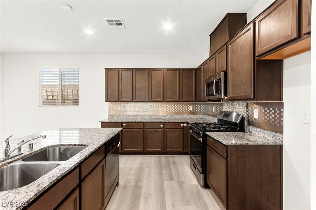 kitchen with visible vents, light stone countertops, a sink, light wood-style floors, and stainless steel appliances