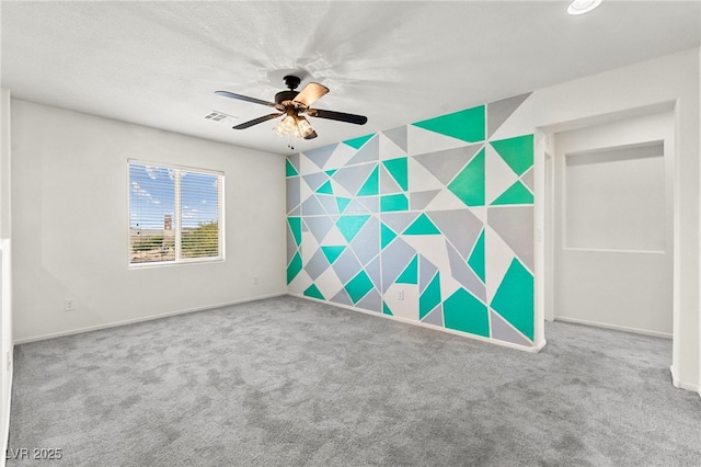 empty room featuring ceiling fan, visible vents, baseboards, an accent wall, and carpet flooring
