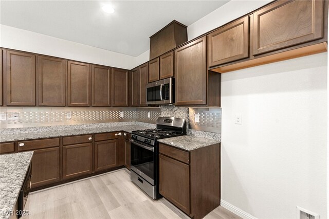 kitchen featuring light wood-style floors, appliances with stainless steel finishes, backsplash, and light stone countertops