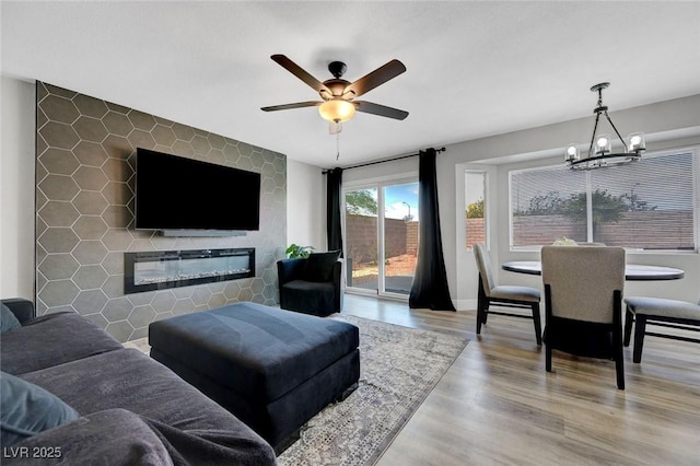 living area with ceiling fan with notable chandelier, a glass covered fireplace, and wood finished floors