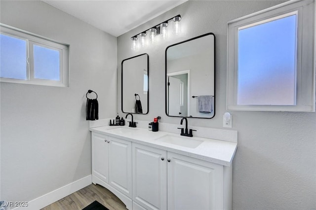 bathroom with a sink, double vanity, baseboards, and wood finished floors