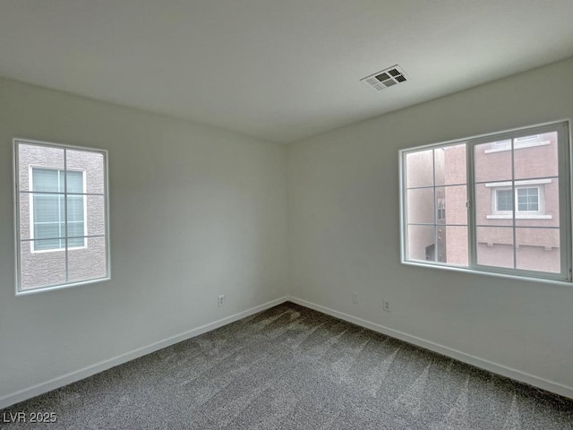 unfurnished room with baseboards, visible vents, and dark colored carpet