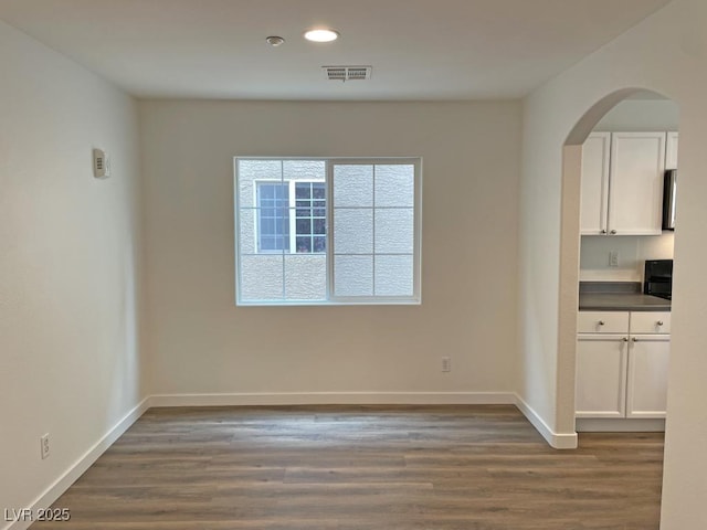 unfurnished dining area with dark wood-style flooring, arched walkways, visible vents, and recessed lighting