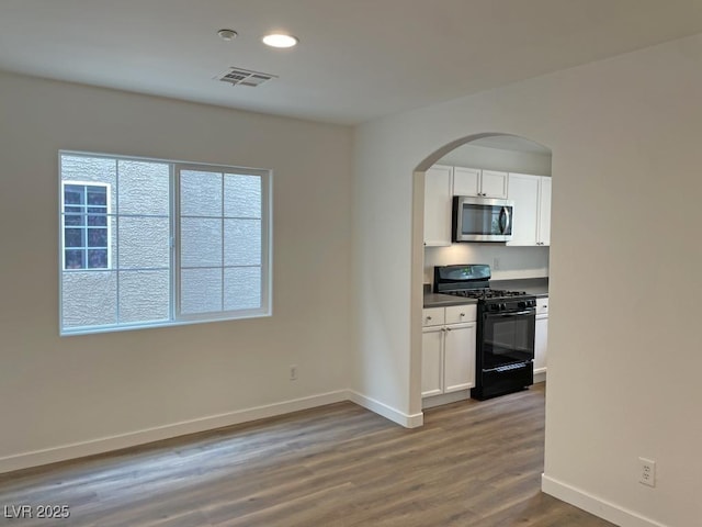 kitchen featuring arched walkways, stainless steel microwave, baseboards, black gas stove, and visible vents