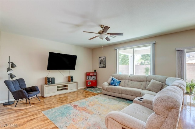 living area featuring baseboards, ceiling fan, wood finished floors, and a wealth of natural light