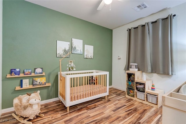 bedroom featuring visible vents, baseboards, a crib, and wood finished floors