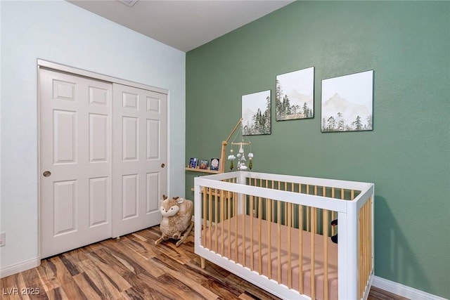 bedroom featuring a crib, baseboards, a closet, and wood finished floors