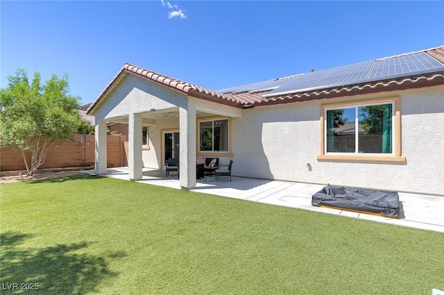 back of property featuring a lawn, fence, roof mounted solar panels, and stucco siding