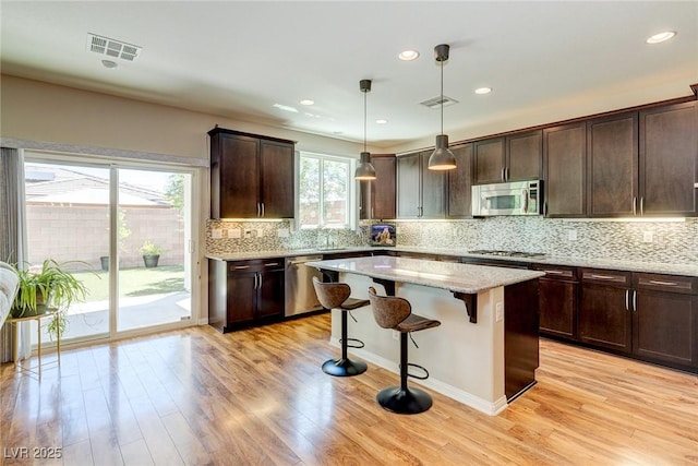 kitchen with stainless steel appliances, dark brown cabinetry, visible vents, and a center island