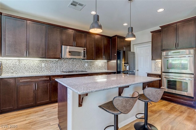 kitchen featuring visible vents, a breakfast bar area, a center island, light wood finished floors, and stainless steel appliances