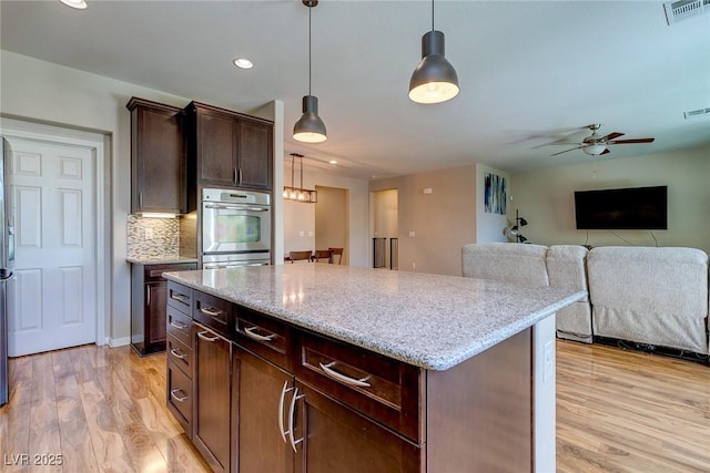 kitchen featuring visible vents, a center island, stainless steel double oven, a ceiling fan, and light wood finished floors