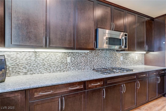 kitchen with appliances with stainless steel finishes, tasteful backsplash, dark brown cabinetry, and light stone countertops