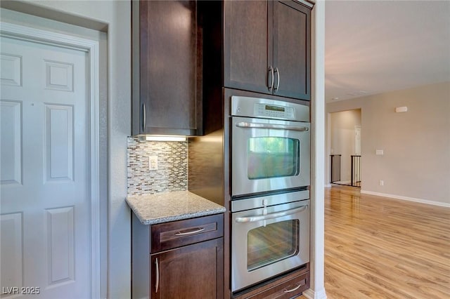kitchen featuring backsplash, stainless steel double oven, light wood-type flooring, dark brown cabinets, and baseboards