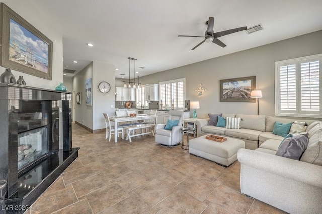 living room with baseboards, a multi sided fireplace, a ceiling fan, and visible vents