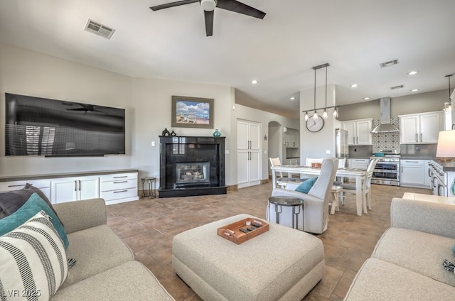 living room with visible vents, a ceiling fan, a glass covered fireplace, and arched walkways
