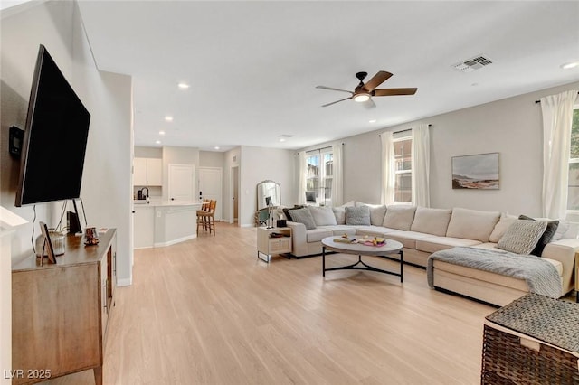 living room featuring light wood-style floors, ceiling fan, a wealth of natural light, and visible vents