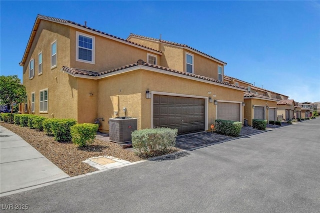 view of front of property featuring an attached garage, central AC unit, a tile roof, and stucco siding