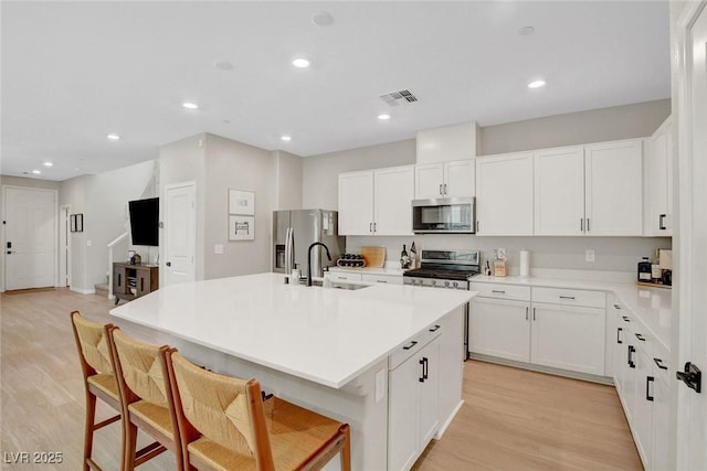 kitchen with visible vents, a kitchen breakfast bar, light wood-type flooring, a sink, and appliances with stainless steel finishes