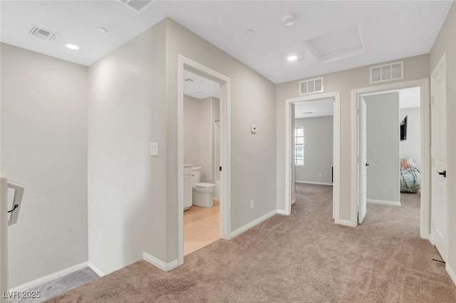 corridor featuring visible vents, attic access, and light colored carpet