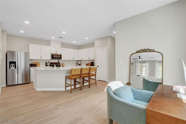 kitchen featuring light wood-style floors, a kitchen breakfast bar, light countertops, white cabinets, and stainless steel appliances