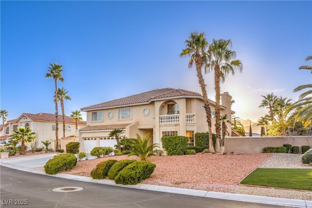 mediterranean / spanish-style home with stucco siding, an attached garage, a tile roof, driveway, and a balcony