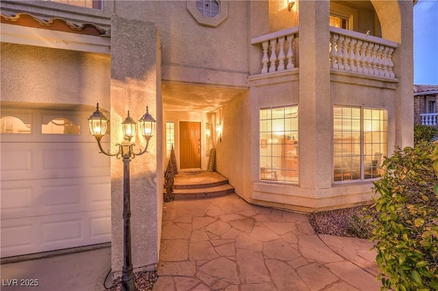 entrance to property with a garage, stucco siding, and a balcony