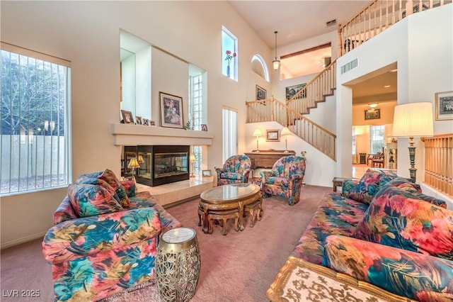 carpeted living area featuring a high ceiling, a glass covered fireplace, and stairway