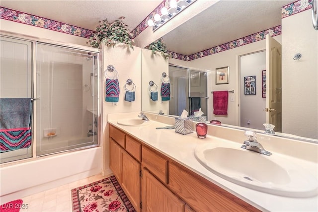 full bathroom with bath / shower combo with glass door, double vanity, and a textured ceiling