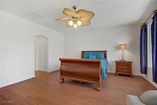 bedroom with arched walkways, a ceiling fan, baseboards, wood finished floors, and visible vents