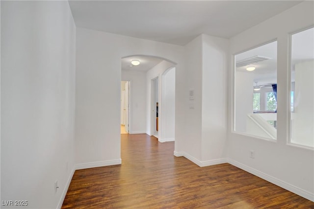 unfurnished room with arched walkways, baseboards, wood finished floors, and visible vents