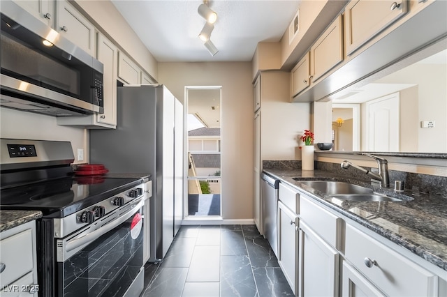 kitchen featuring a sink, rail lighting, dark stone counters, stainless steel appliances, and visible vents