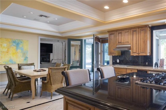 kitchen with crown molding, brown cabinetry, tasteful backsplash, under cabinet range hood, and visible vents