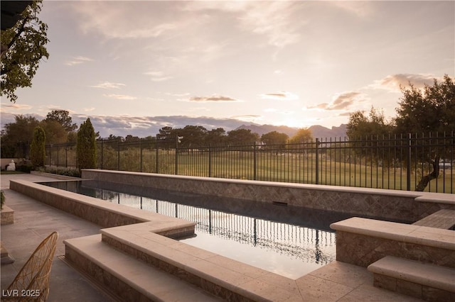 pool at dusk with a fenced backyard and a fenced in pool