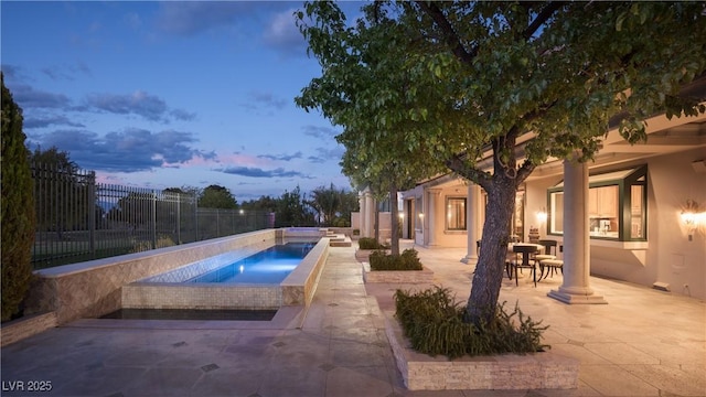 pool at dusk featuring a patio, an in ground hot tub, fence, and a fenced in pool