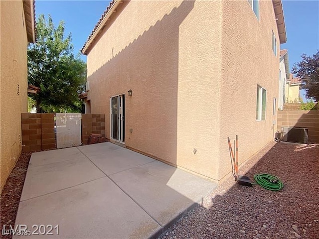 view of side of property with fence, a gate, a patio, and stucco siding