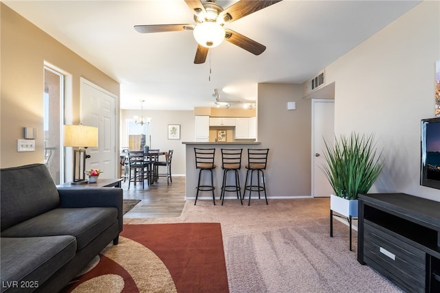 living room with carpet floors, ceiling fan with notable chandelier, baseboards, and visible vents