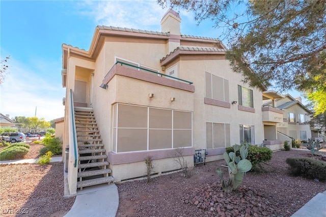 exterior space with a tiled roof, stucco siding, stairway, and a chimney