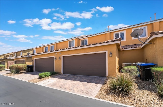 townhome / multi-family property with decorative driveway, stucco siding, central AC unit, a tiled roof, and an attached garage