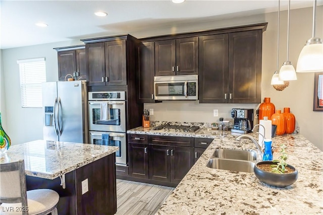kitchen featuring dark brown cabinets, light stone counters, hanging light fixtures, a sink, and stainless steel appliances