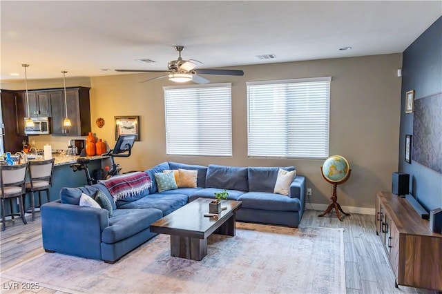 living area with visible vents, light wood finished floors, ceiling fan, and baseboards