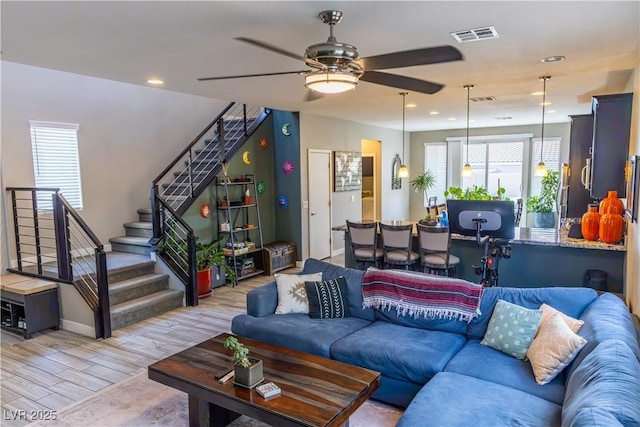 living room with stairs, ceiling fan, visible vents, and light wood-style floors