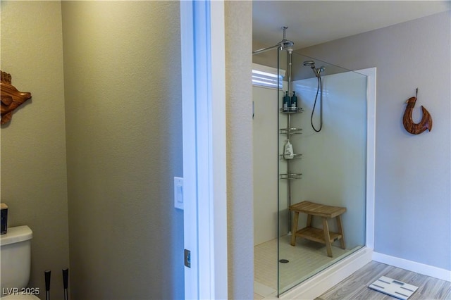 bathroom with toilet, wood finished floors, and a stall shower