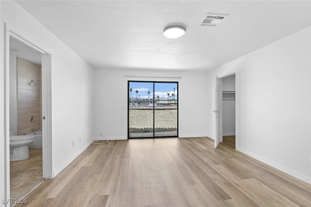 unfurnished bedroom featuring baseboards, ensuite bath, light wood-style flooring, and visible vents