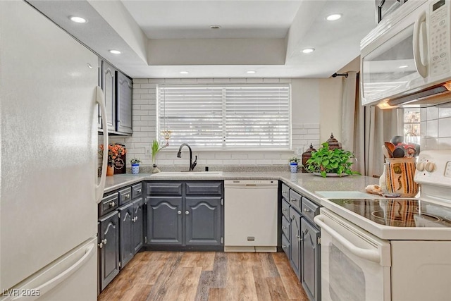 kitchen with gray cabinetry, a sink, backsplash, and white appliances